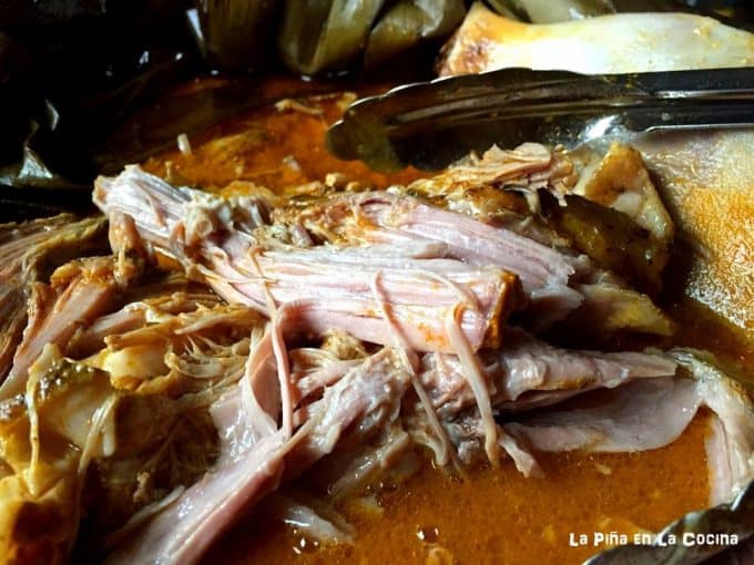 Pulling slow roasted pork with tongs from roasting pan