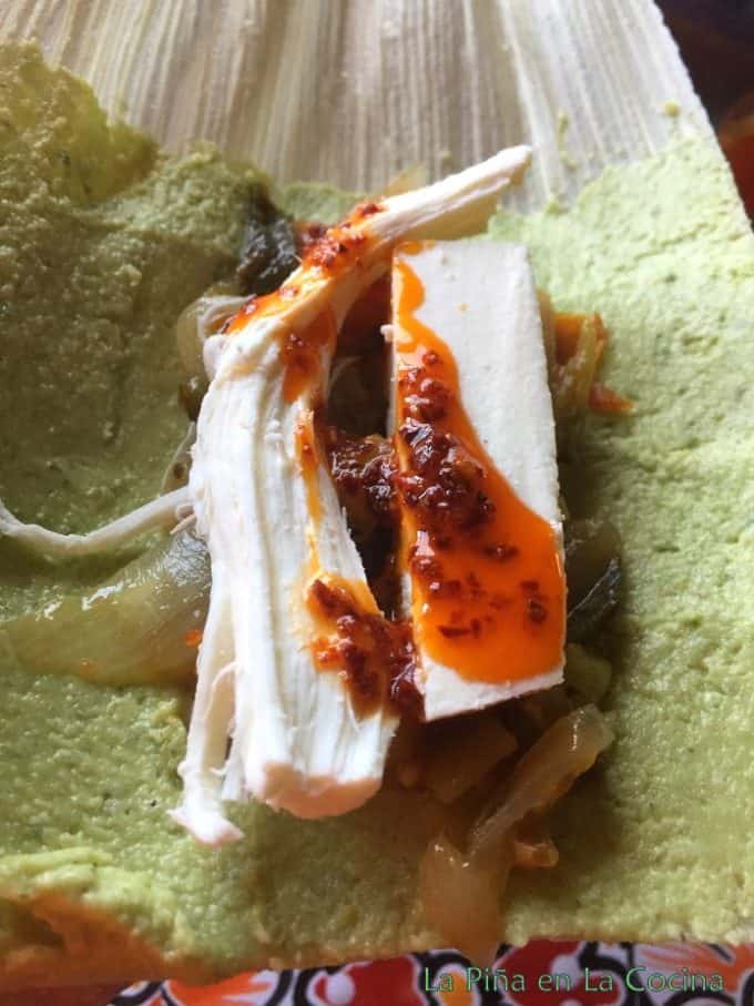 Open uncooked tamal with masa, filling and spoonful of salsa macha