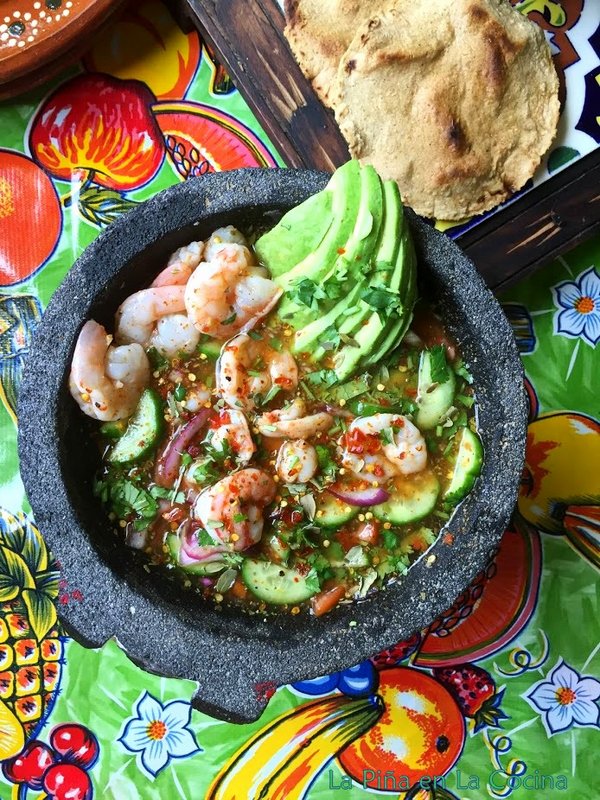 Top view of chile piquin shrimp aguachile in the Mexican molcajete, Two corn tostadas on the side.