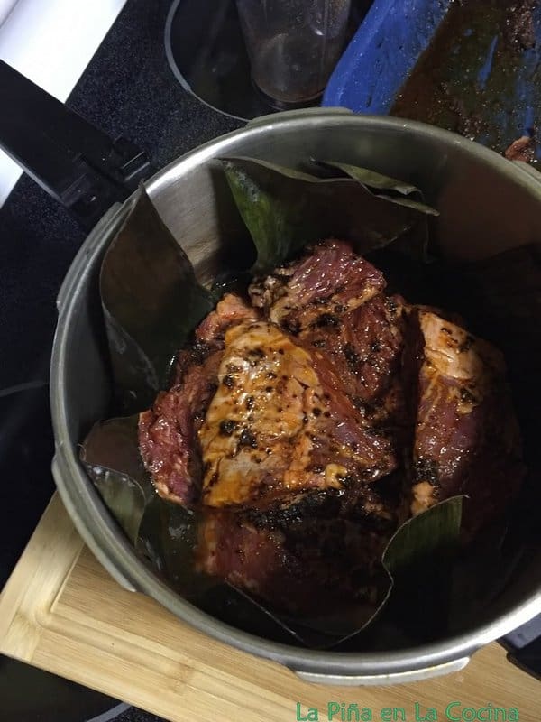 Seasoned beef in pressure cooker that is lined with banana leaves 