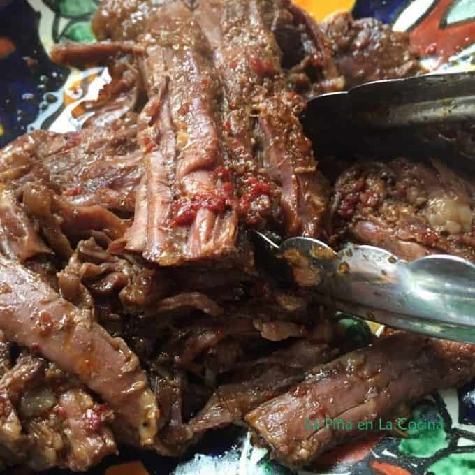 Barbacoa shredded in a bowl close up with tongs
