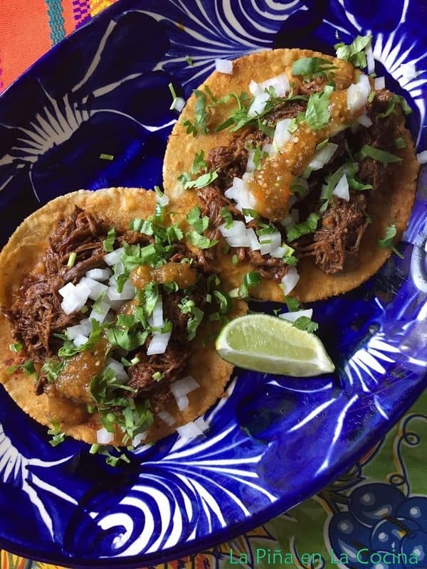 Two barbacoa tacos garnished with fresh ingredients on a blue Mexican plate