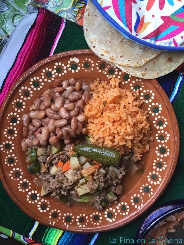 Picadillo plated with pinto beans and Mexican rice. Flour tortillas in warmer