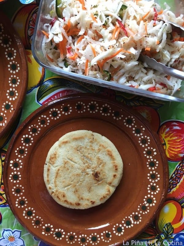 Pupusa on a plate by itself. Cabbage in storage conatainer on the side.