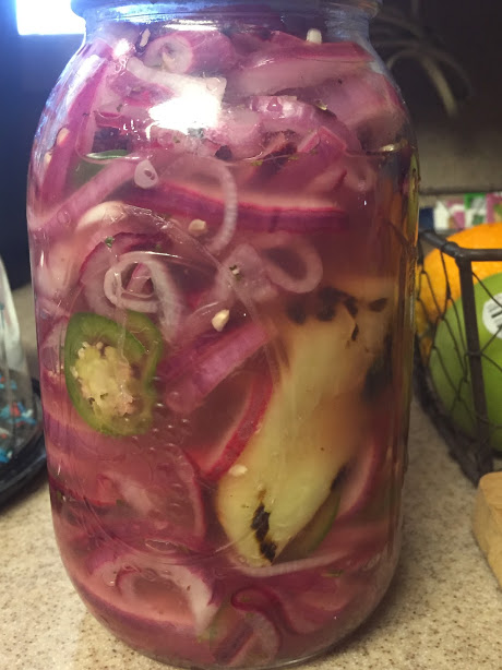 Pickled red onions in a jar with a charred chile pepper