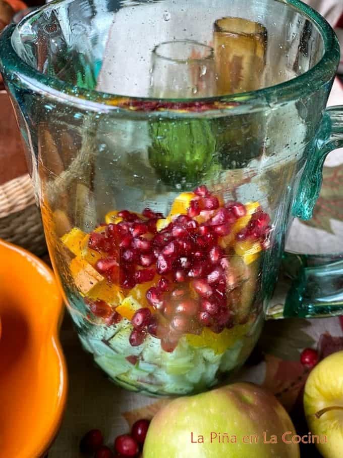 Pitcher filled with apples, oranges and pomegranate seeds