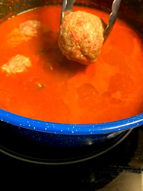 Transferring uncooked meatballs into red salsa in pot