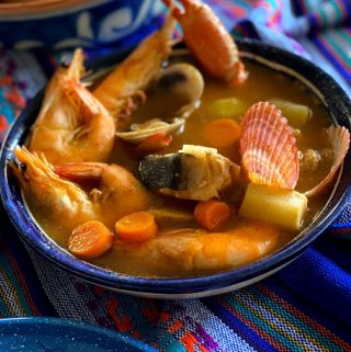 seafood soup in a large deep bowl with bowls of garnish and bread on the table