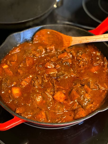 beef and potato simmering in skillet with wooden spoon on one side