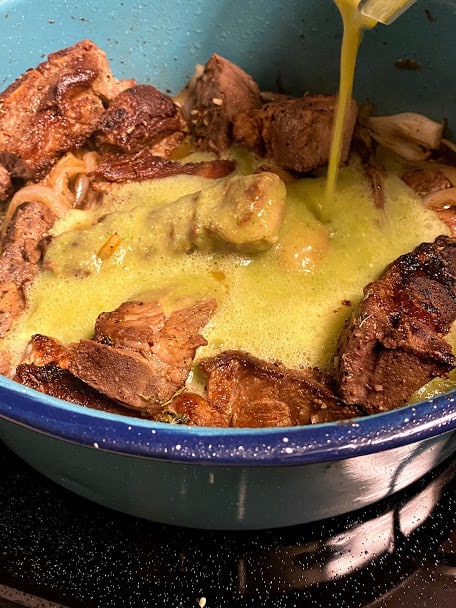Pouring in freshly blended salsa verde into pan with ribs