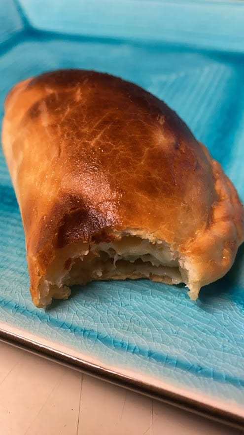 close up of one empanada on blue plate. Empanada has a bite taken out of the end