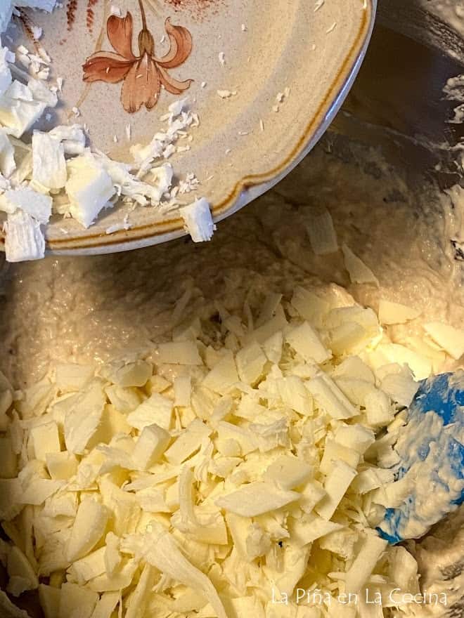 Adding chopped pieces of Oaxaca cheese to the sticky dough in the bowl