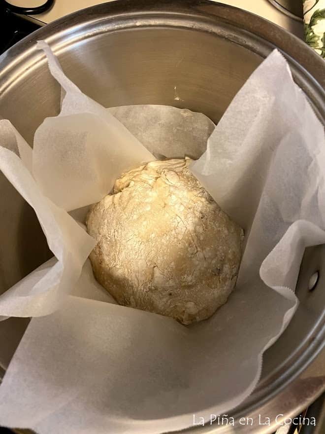 Unbaked bread loaf in deep stainless steel pot with parchment paper ready for the oven