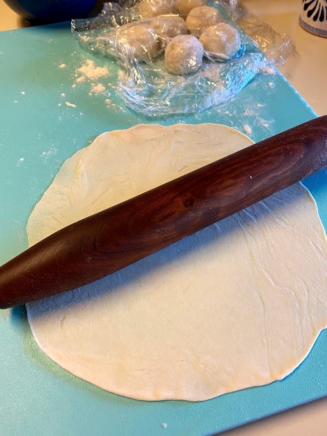 rolled out flour tortilla on cutting board with rolling pin
