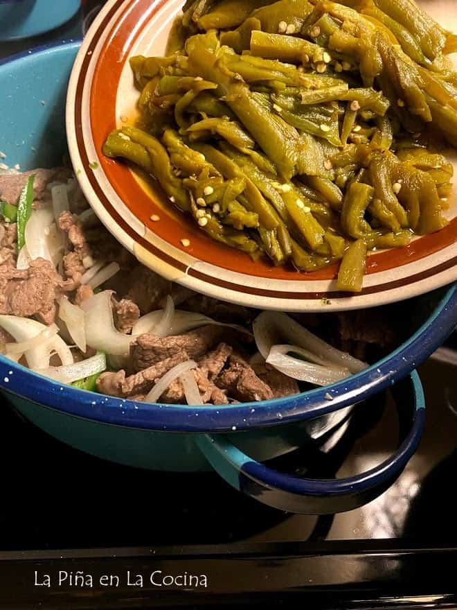 big plate of green chile strips going into the pot of beef on stove top