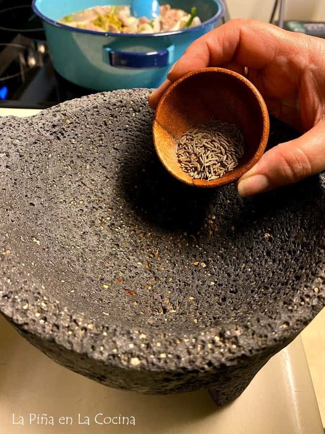 a lava stone Mexican molcajete with me holding a tiny bowl of cumin seeds