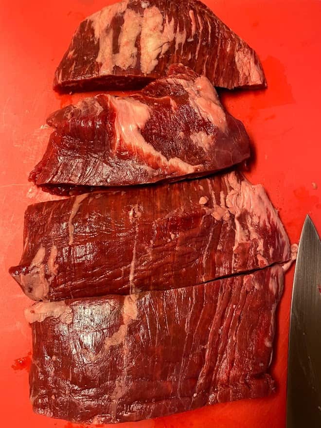 flank steak sliced into 4 sections raw on cutting board