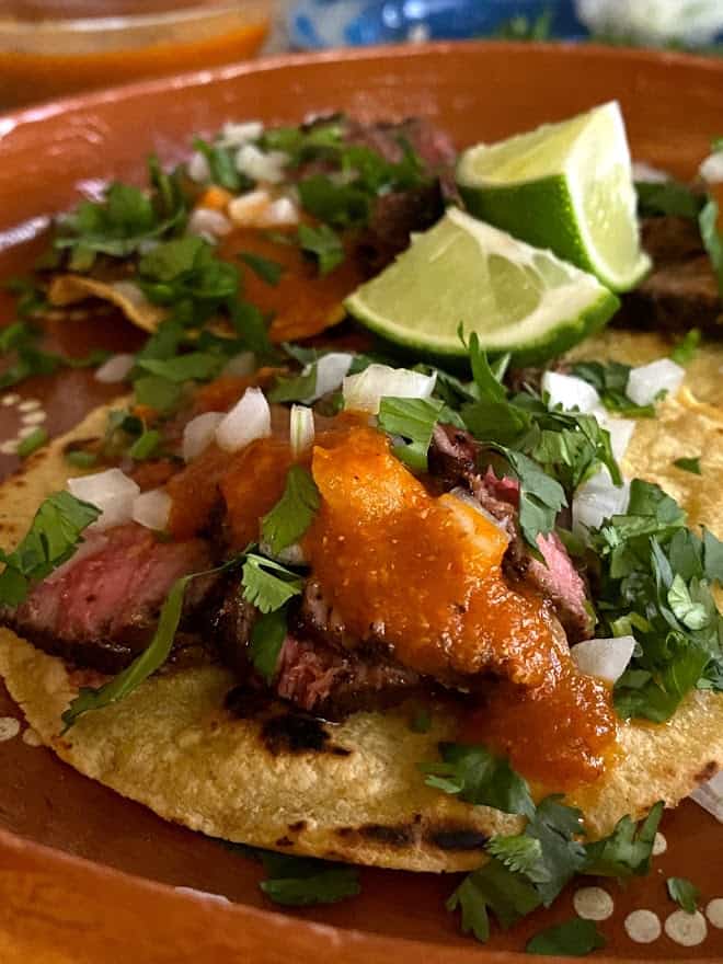 close up of flank steak tacos with salsa and fresh garnishes