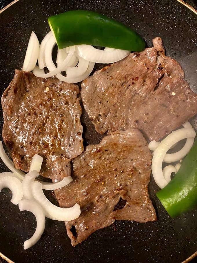 thin skirt steak searing in skillet with onions and jalapeños