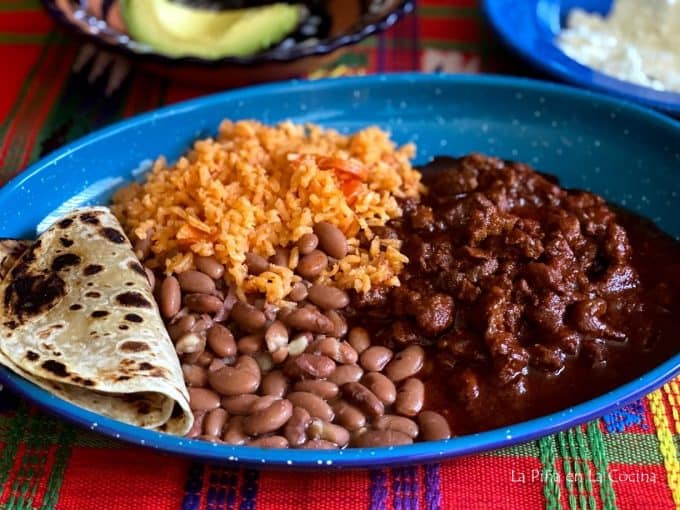 landscape view of plated carne con chile served with rice, beans and tortillas