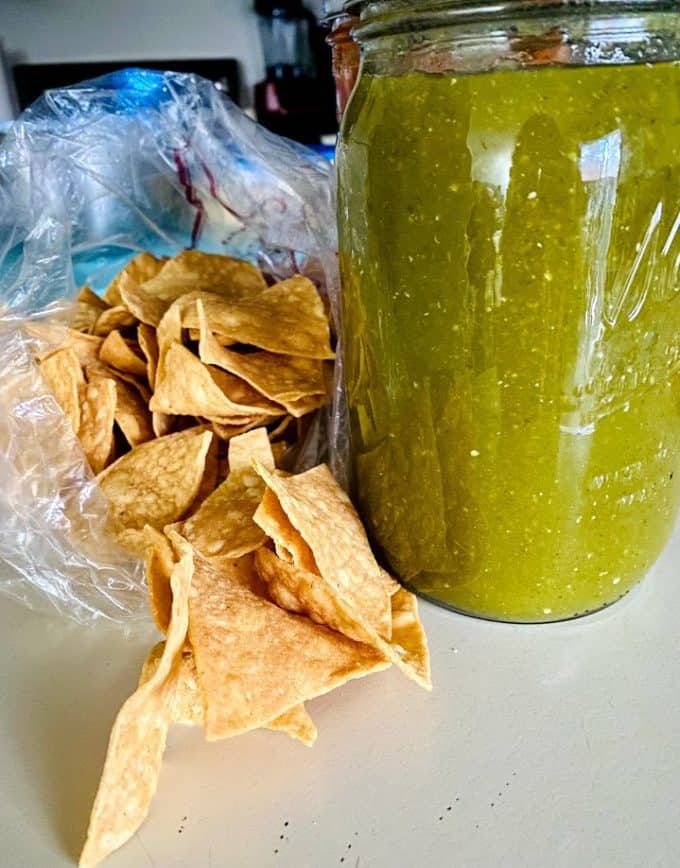 Salsa verde in a tall mason jar with tortilla chips on the side