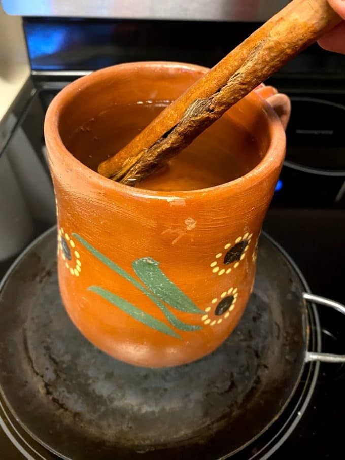 clayware pot filled with water, cinnamon stick, piloncillo and orange peel on the stove top