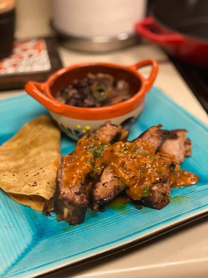 pork ribs plated with spucy salsa, corn tortillas, beans