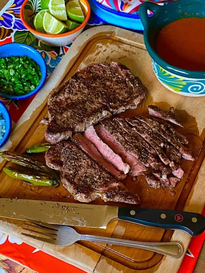 sliced steak on board with salsa and fresh garnishes in bowls