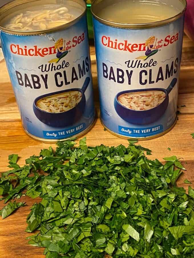 two cans of baby clams open on top, fresh parsley on the side