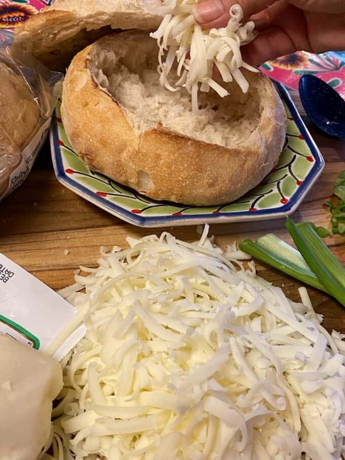 adding shredded jack cheese to bottom of bread bowl