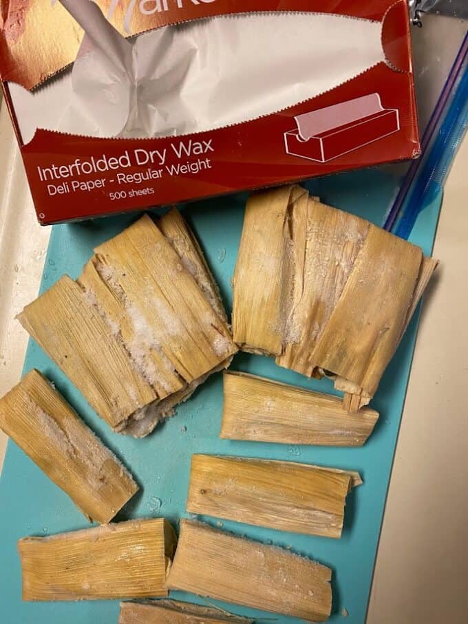 uncooked frozen tamales on cutting board with box of deli paper sheets