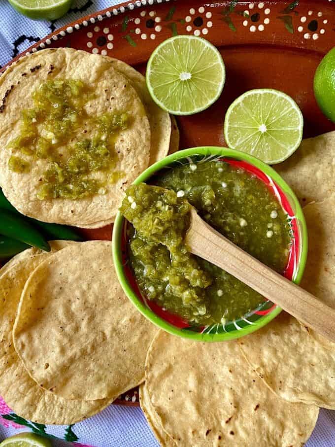 top view of salsa in a bowl with wooden spoon, tostadas, sliced limes