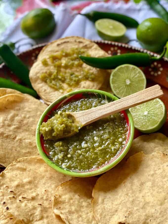 Serrano Lime Salsa in small bowl with wooden spoon, corn tostadas and limes