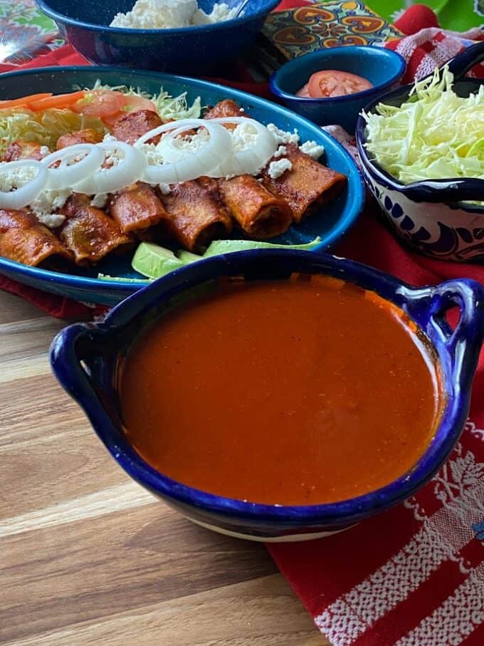 enchilada sauce in the front, plate of enchiladas in the back