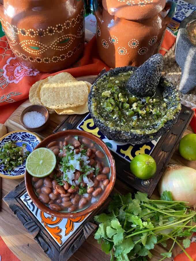 bowl of pinto beans, salsa in molcajete, fresh ingredients, corn tostadas