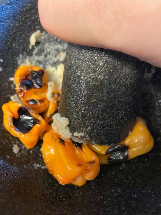 grinding roasted habanero peppers with garlic in the molcajete