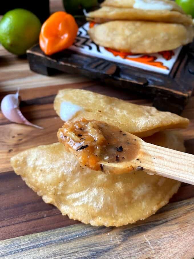 habanero salsa in small wooden spoon over fried empanada