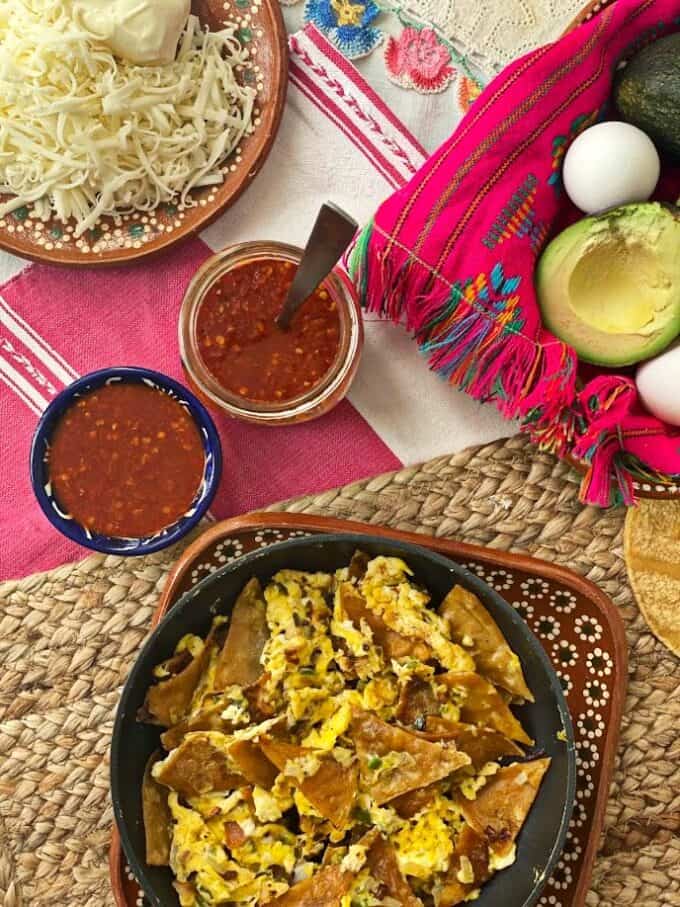 arbol hot sauce with migas in skillet, plate of shredded cheese, avocado, eggs