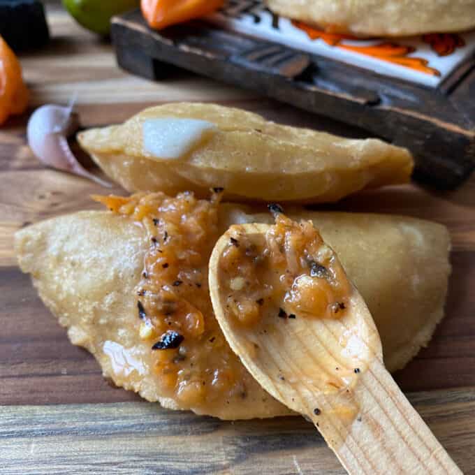 habanero salsa on wooden spoon with fried corn masa empanadas