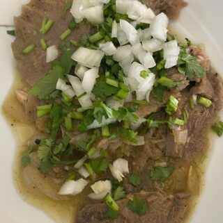 beef tongue in salsa garnished with cilantro and onion