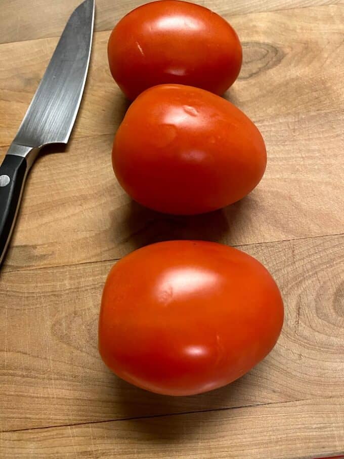 three roma tomatoes on cutting board