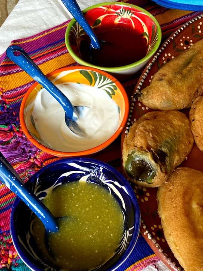 close up of salsas and crema in small bowls, rellenos on one side