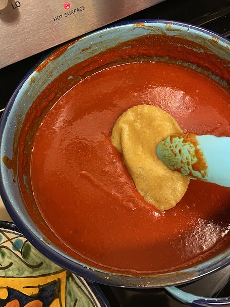 dipping fried tortilla into enchilada sauce