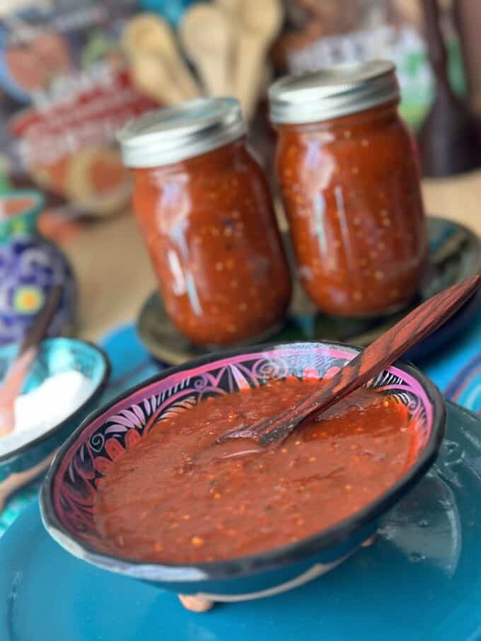 red salsa in a bowl with 2 mason jars filled in the back
