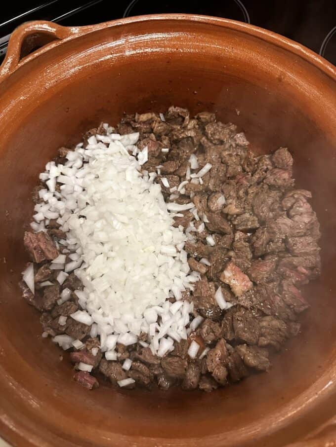 adding diced onions to beef in large cazuela