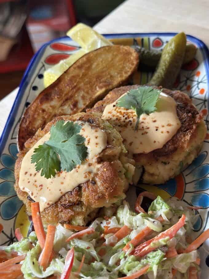 crab cakes plated with slaw and fried potato wedges