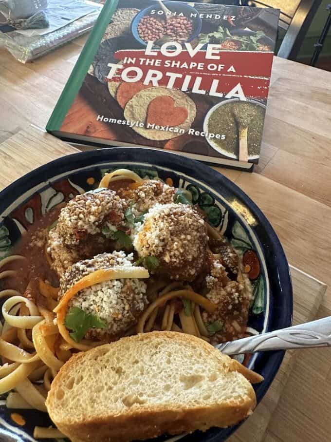 meatballs with red sauce and pasta plated, bread, mexican salsa cookbook on one side
