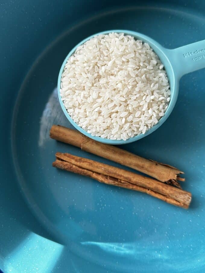 medium grain rice in measuring cup with 2 large cinnamon sticks
