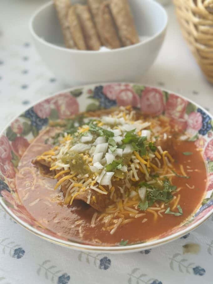 plated taquitos en caldillo with shredded cheese, salsa verde, cilantro and onion
